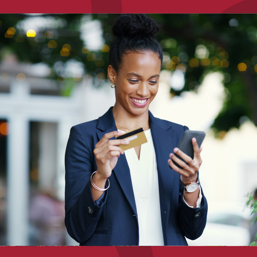 A woman is smiling while holding her cell phone in one hand and a credit card in the other.